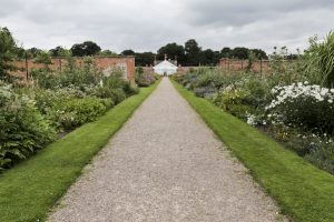 The view from the south gate up to the middle section of the glass house. The gravel path is in the centre of the walled garden and runs from the gate to the glass house past plots of plants, fruits, veg.