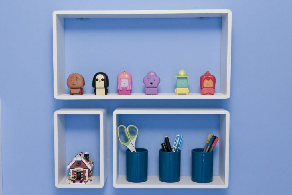 Close up of B & Q White Cube Shelves fitted to blue bderoom wall and filled with Emily's ornaments and pens, pencils and ornaments