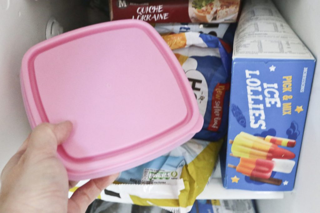 Puting a tupperware container filled with food into the freezer