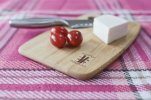 The smallest bamboo chopping board shown with cheese, tomatoes and a knife.
