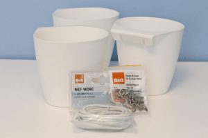 Three Ikea Bygel containers in a cluster on a desk with a packet of B&Q hooks and Eyes and B&Q net curtain wire.