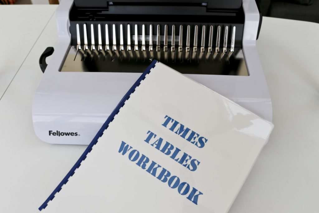 The completed bound times table workbook in front of the Fellowes Pulsar 300 Comb Binder Lid Closed