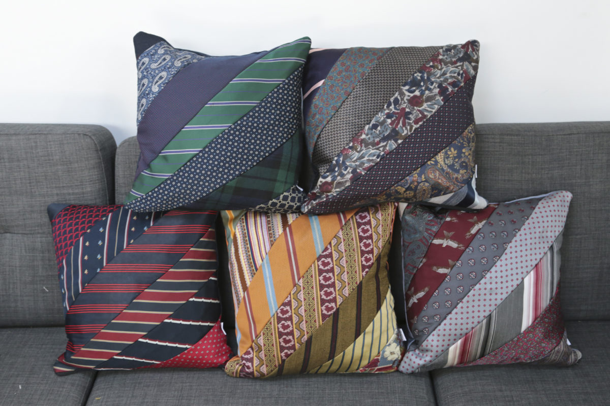 5 different colour schemes of cushions made from neck ties stacked on a sofa.