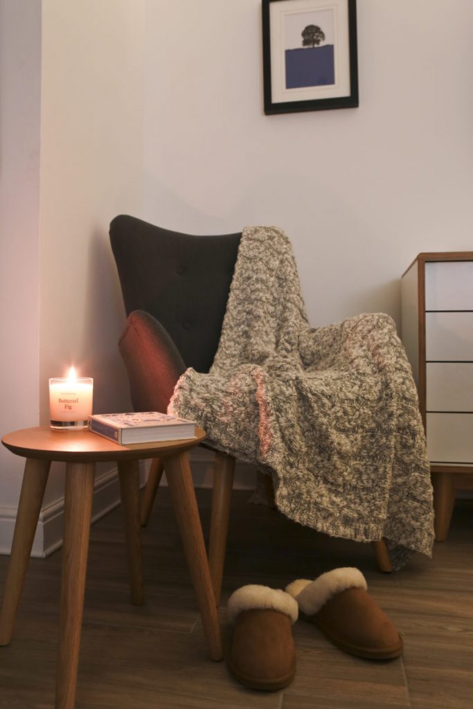 Ultimate Hygge with a cosy corner chair, slippers, candle, book and throw