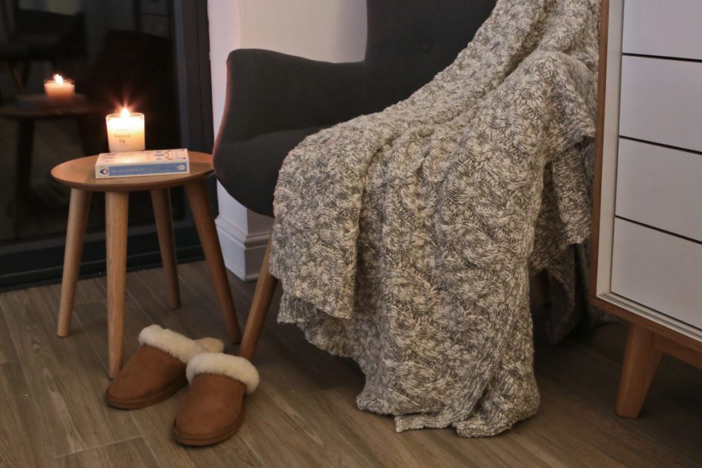 Ultimate Hygge with a cosy corner chair, slippers, candle, book and throw