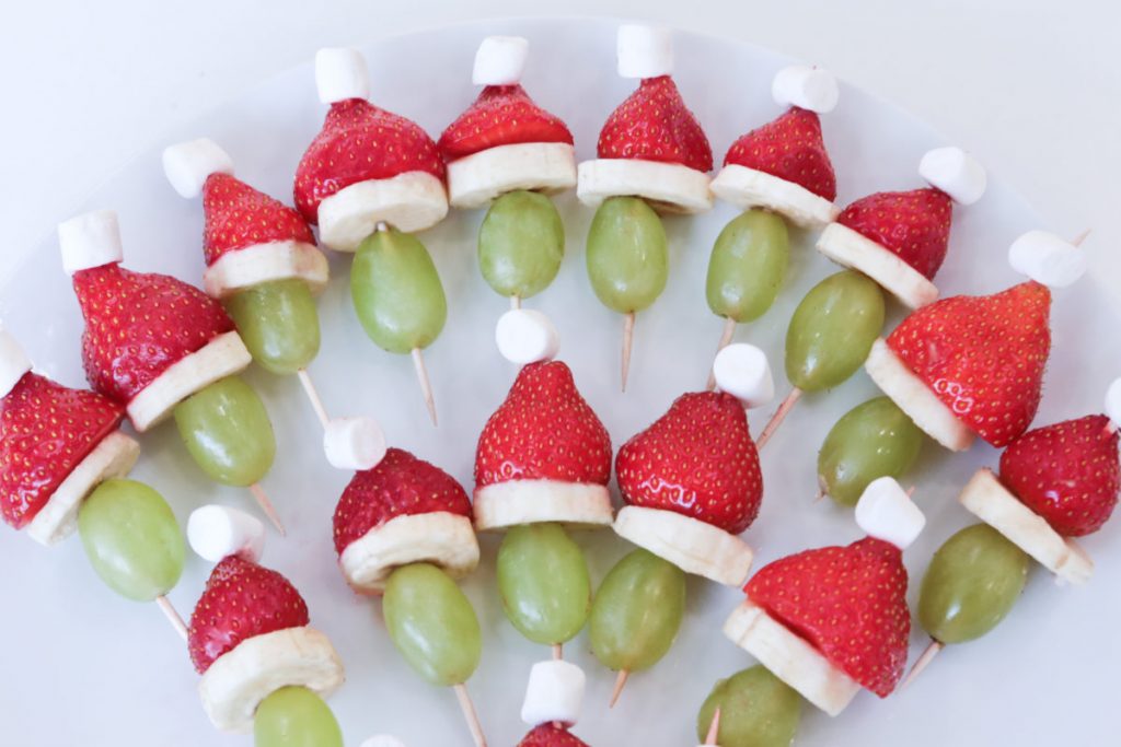 Christmas food and recipe ideas: fun, festive and delicious treats which are perfect for making with kids. White chocolate coated pretzels with green and red sugary sprinkles and Santa Hat fruit skewers