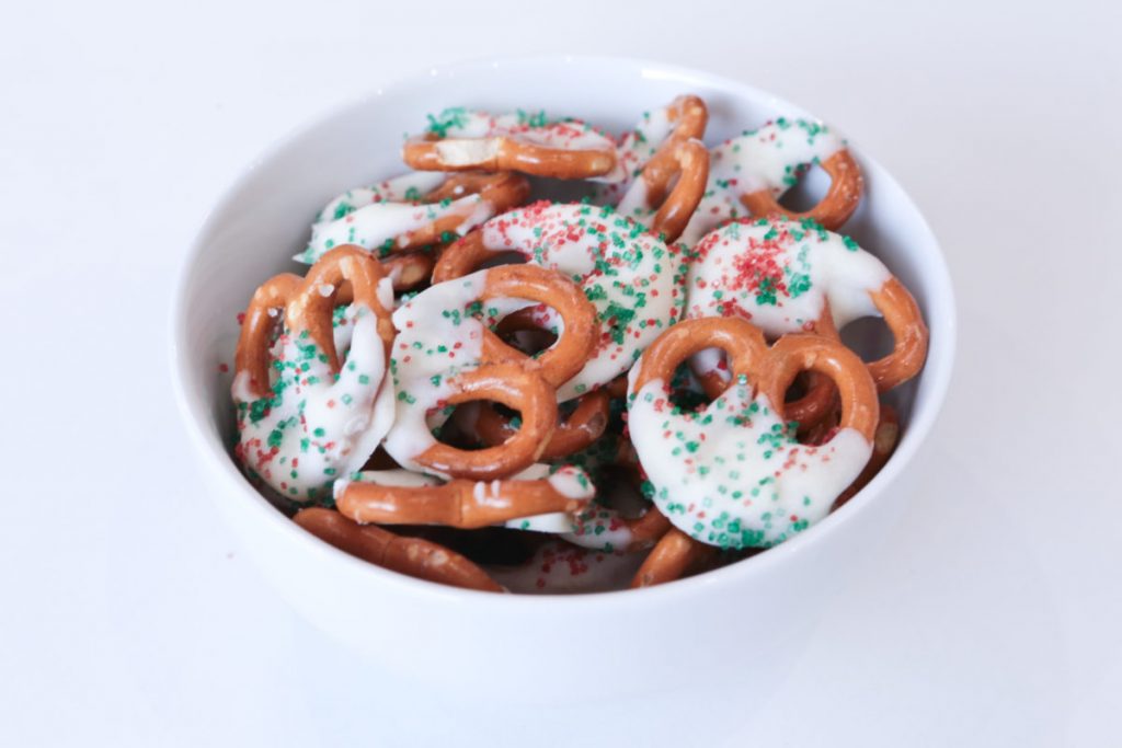 A bowl of pretzels coated in white chocolate with green and red sugary sprinkles on top
