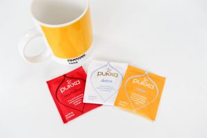 Pukka Herbal Tea sachets next to a Pantone mug